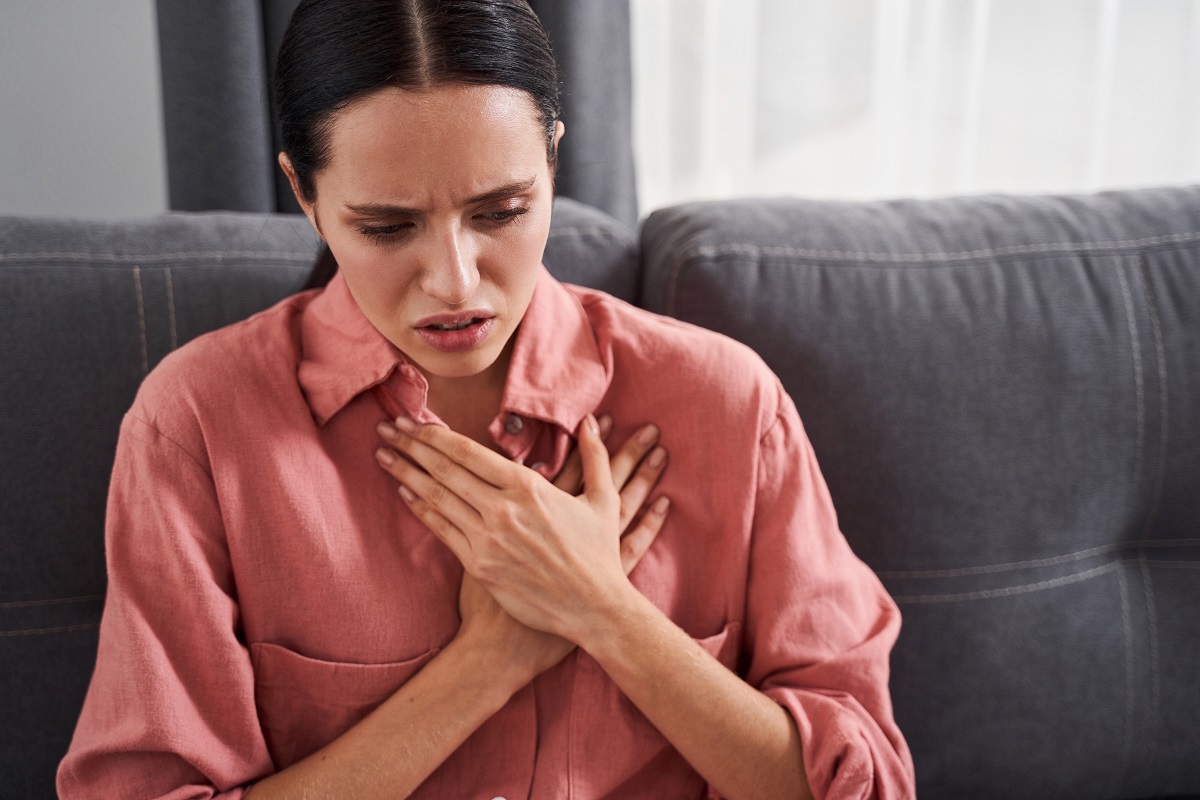 O femeie brunetă și slabă se ține cu ambele mâini de piept, ceva îi afectează sănătatea inimii