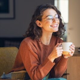 O femeie frumoasă cu părul creț și ochelari care savurează o cană de ceai, fiind pe lista de băuturi care te ajută să ai un abdomen plat