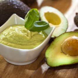 Un avocado tăiat în două, lângă un bol cu pastă de avocado sugerează beneficiile consumului acestui fruct
