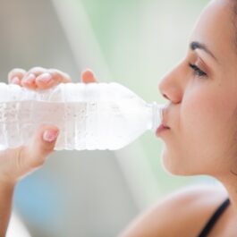 O femeie tânără bea apă dintr-o sticlă de plastic transparentă