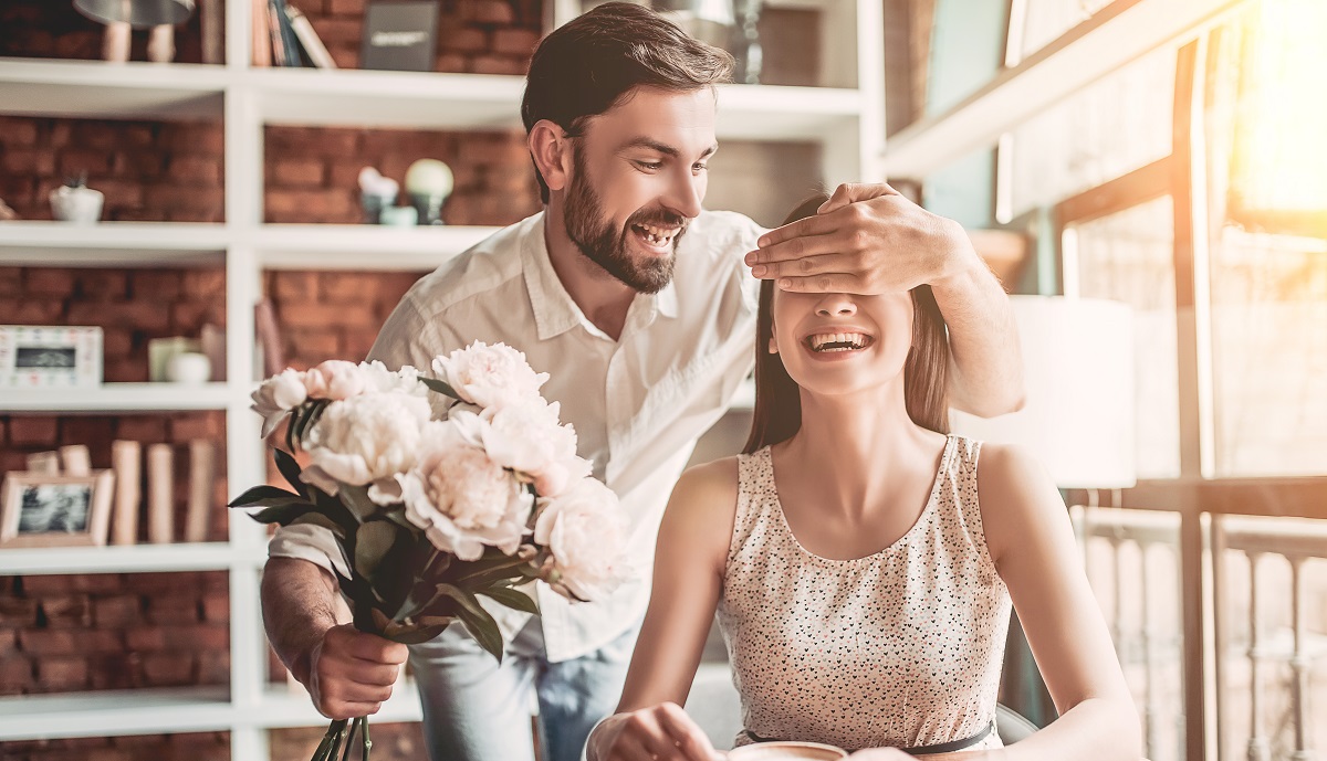 Un cuplu fericit care se află la o cafenea, în timp ce bărabtul îi oferă iubitei sale un buchet de flori
