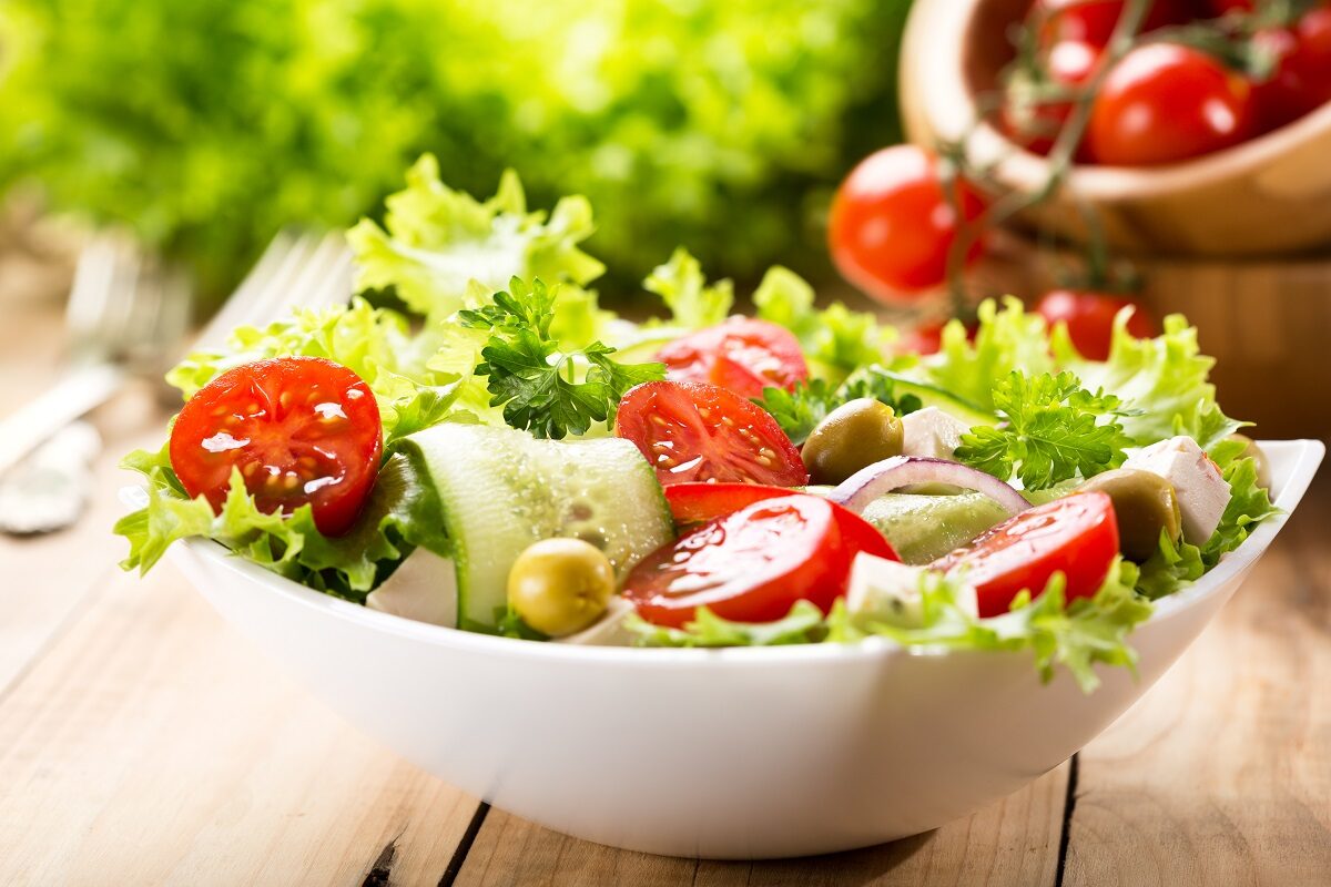 Un bol de ceramică alb plin cu salată verde și alte legume specifice unei alimentații sănătoase