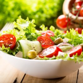 Un bol de ceramică alb plin cu salată verde și alte legume specifice unei alimentații sănătoase