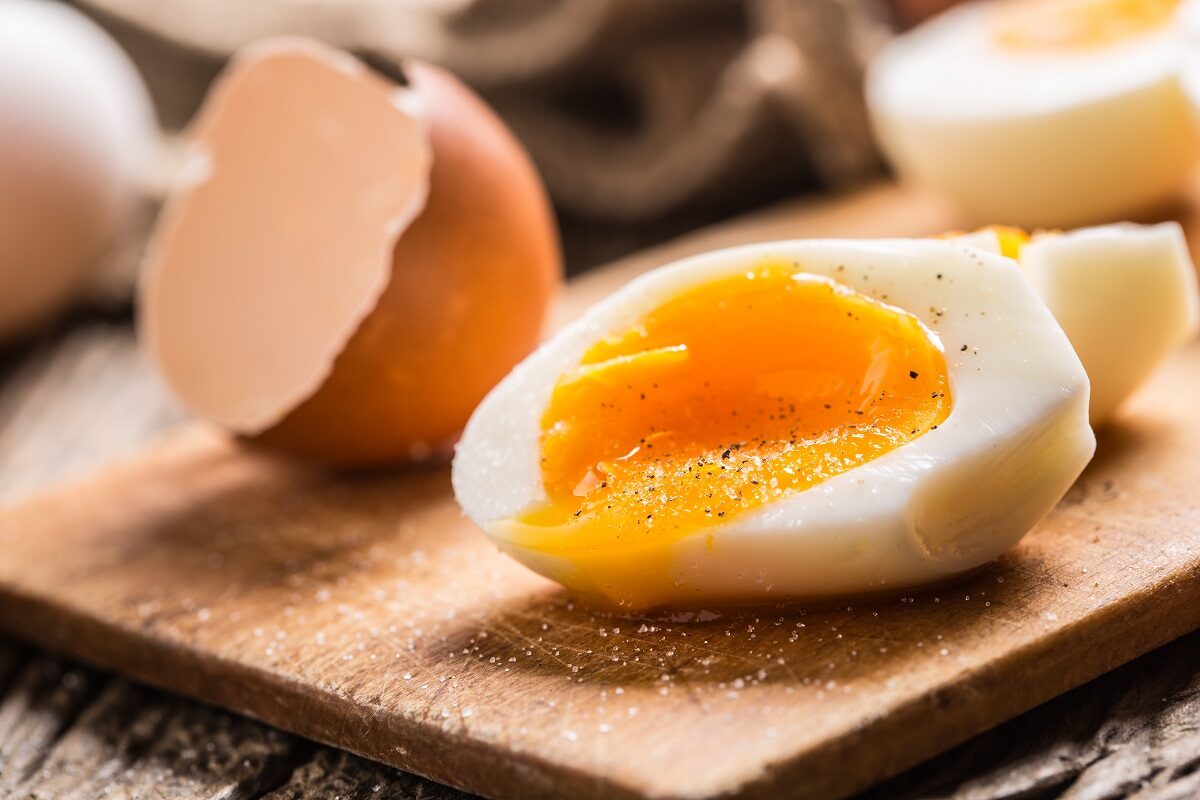 Un ou fiert tăiat pe jumătate care stă pe un tocător de lemn pentru a ilustra ce se întâmplă în corpul tău dacă mănânci ouă timp de o săptămână