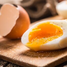 Un ou fiert tăiat pe jumătate care stă pe un tocător de lemn pentru a ilustra ce se întâmplă în corpul tău dacă mănânci ouă timp de o săptămână