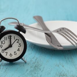 Un ceas desteptător de culoare neagră, alături de o farfurie albă, goală sugerează ce se întâmplă în organism dacă sari peste mese