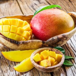 Imagine cu un mango copt întreg și unul feliat și unul cubulețe, într-un coșuleț maro