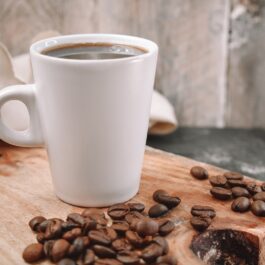 O cană albă de cafea neagră pe un blat de lemn sugerează o metodă simplă despre cum să fii prietenoasă cu mediul înconjurător dacă bei cafea