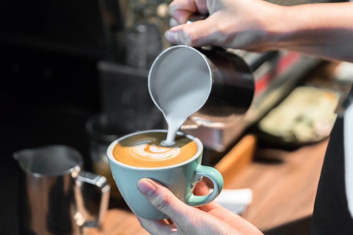 O barista prepară o ceașcă de cafea cu lapte, formând în mijloc o inimă din spumă