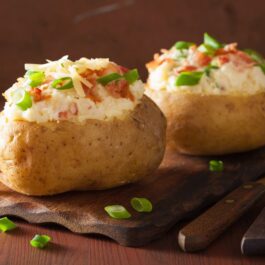 Cartofi umpluți cu brânză și condimente decorați cu bucăți de bacon și rondele de ceapă verde