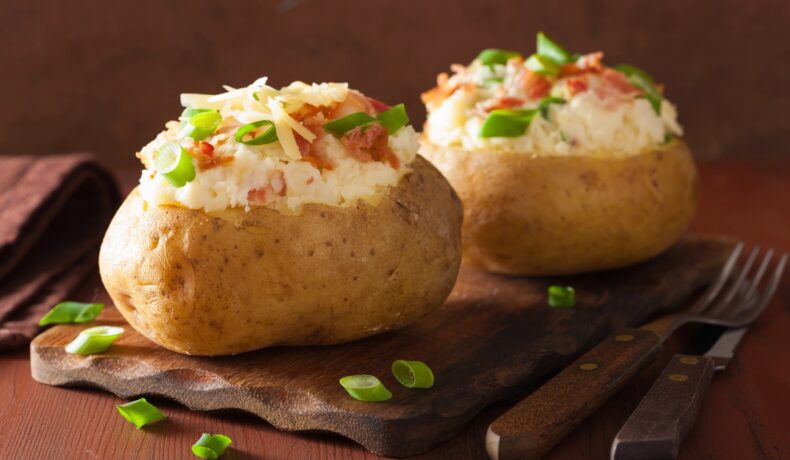 Cartofi umpluți cu brânză și condimente decorați cu bucăți de bacon și rondele de ceapă verde