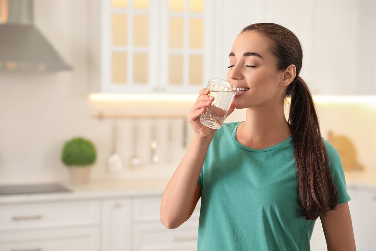 O femeie frumoasă care poartă un tricou albastru și bea un pahar mare cu apă