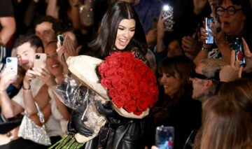 Kourtney Kardashian și Travis Barker, în primul rând, la o prezentare de modă, cu ea ținând în brațe un buchet mare de trandafiri