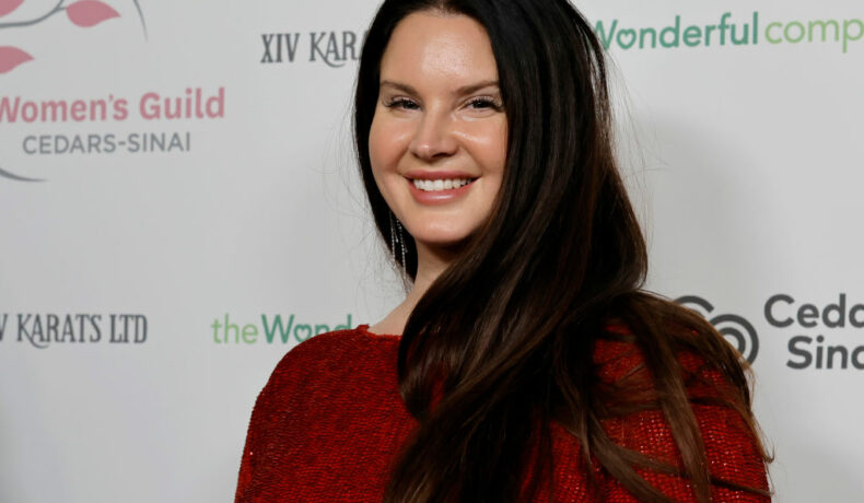 Lana Del Rey, zâmbitoare, într-o rochie roșie, la un eveniment