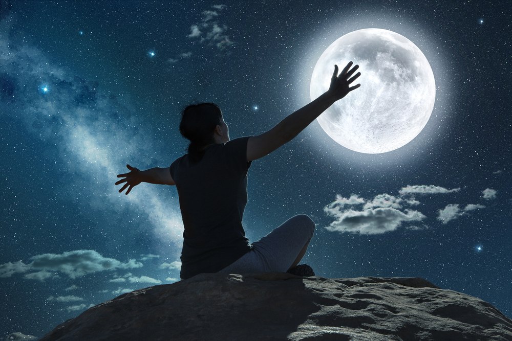 Fată stă cu fața către lună și cu mâinile întinde către aceasta