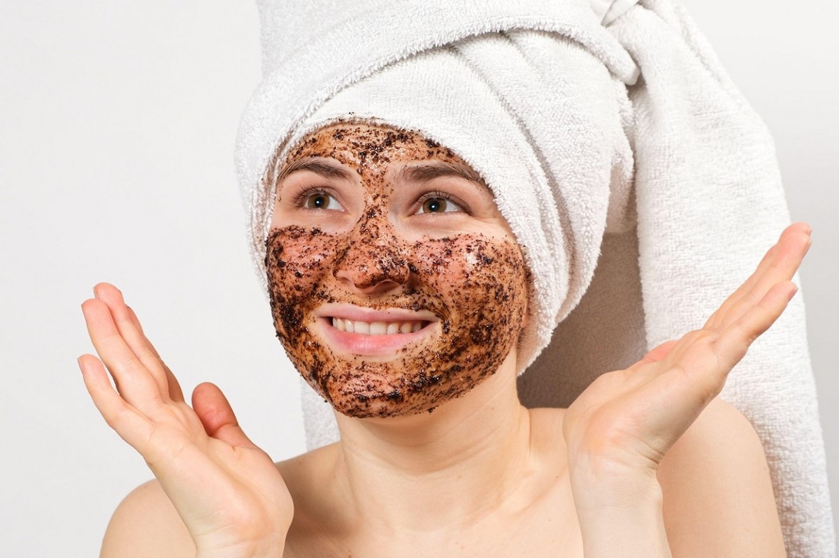 O femeie tânără și zâmbitoare și-a aplicat o mască din zaț de cafea pe față