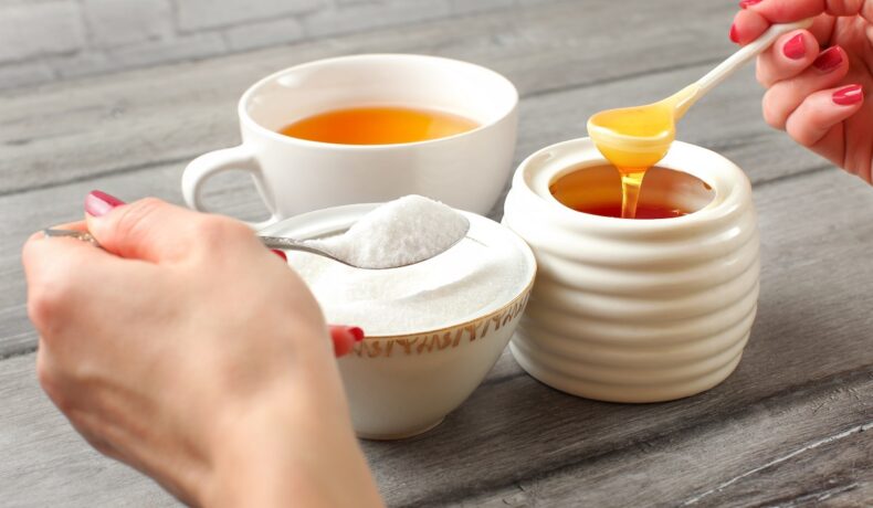 O imagine care sugerează că mierea poate fi un înlocuitor al zahărului pentru că este prezentată o cană de ceai albă, alături de două recipiente albe de ceramică ce conțin zahăr și miere.