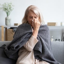 O femeie cu vârsta în jurul a 50 de ani este răcită și stă pe o canapea, cu o pătură pe ea fiindcă nu a respectat obiceiuri care protejează imunitatea în sezonul rece