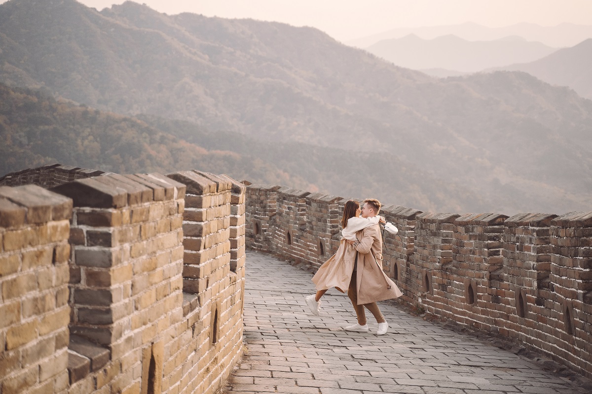 O fotografie panoramică ce surprinde un cuplu care se ține în brațe pe Marele Zid Chinezesc