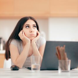 O femeie tânără și brunetă se află în fața unui laptop, dar nu reușește să se concetreze, unul dintre motivele pentru care procrastinarea poate fi un semn al problemelor serioase de sănătate