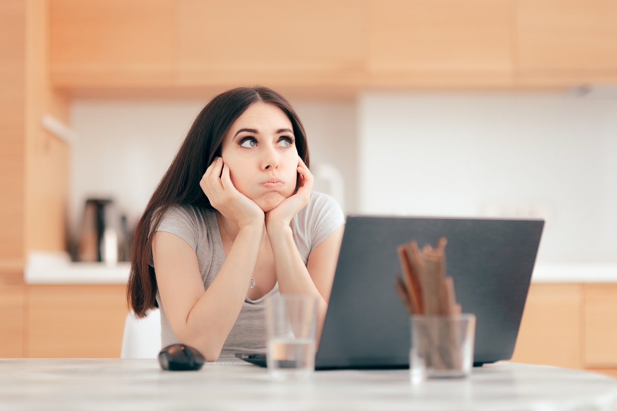 O femeie tânără și brunetă se află în fața unui laptop, dar nu reușește să se concetreze, unul dintre motivele pentru care procrastinarea poate fi un semn al problemelor serioase de sănătate