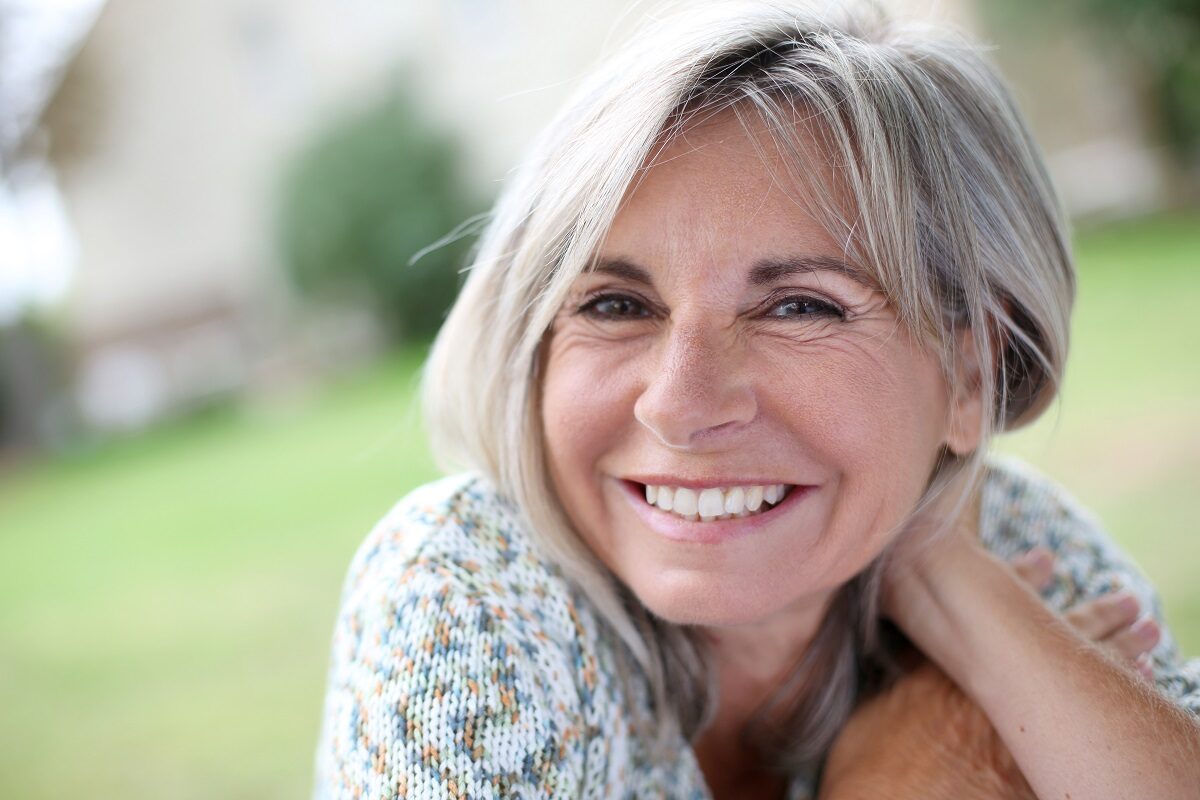 O femeie de peste 50 de ani care zâmbește larg respectă rutina de dimineață pentru femeile cu vârsta de peste 50 de ani