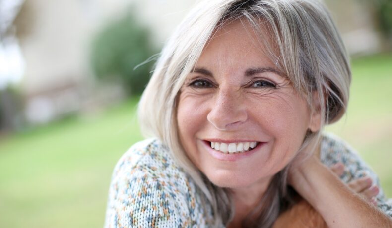 O femeie de peste 50 de ani care zâmbește larg respectă rutina de dimineață pentru femeile cu vârsta de peste 50 de ani