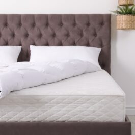 Un pat de culoare gri care are o saltea și așternuturi albe sugerează sfaturi pentru curățarea saltelei