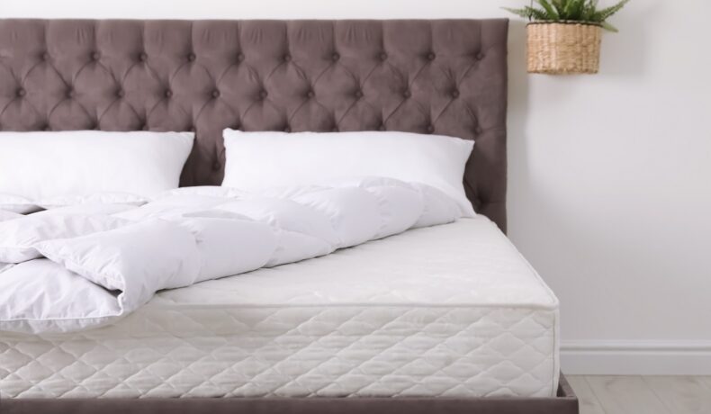Un pat de culoare gri care are o saltea și așternuturi albe sugerează sfaturi pentru curățarea saltelei