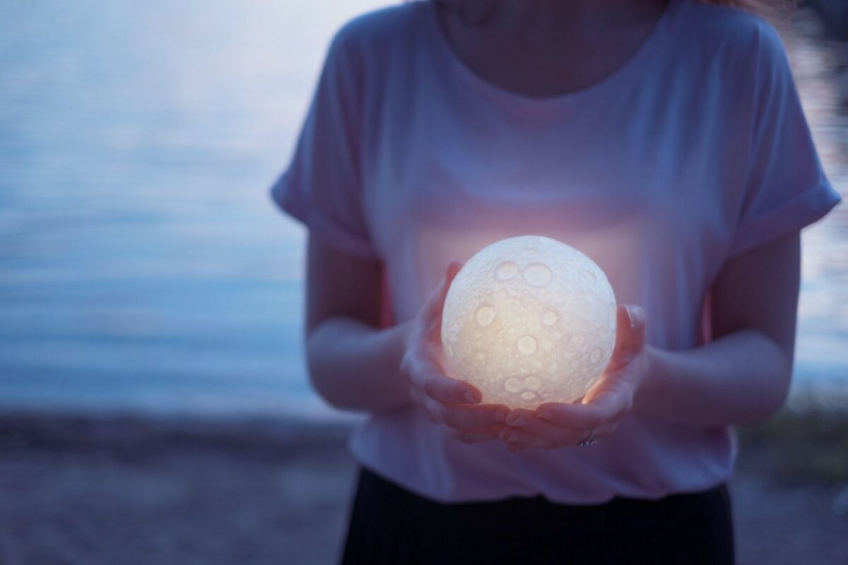 Fată îmbrăcată într-un tricou stă pe plajă și ține în mână o lună mică