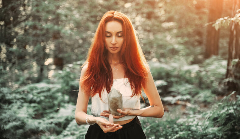 Fată frumoasă cu părul roșu desprins stă într-o pădure cu câteva cristale în mână
