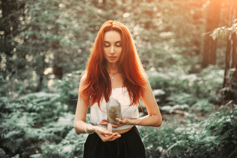 Fată frumoasă cu părul roșu desprins stă într-o pădure cu câteva cristale în mână