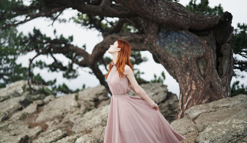 Fată frumoasă îmbrăcată într-o rochie roz pal lungă stă într-o pădure
