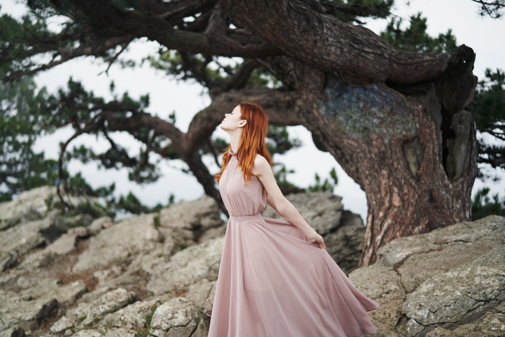 Fată frumoasă îmbrăcată într-o rochie roz pal lungă stă într-o pădure