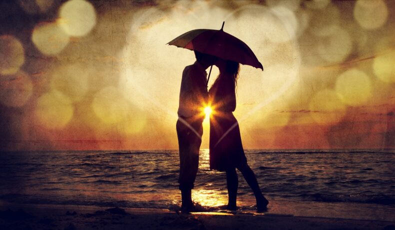 Un cuplu de îndrăgostiți care se sărută la apus pe o plajă pentru a ilustra una dintre cele trei zodii norocoase în dragoste