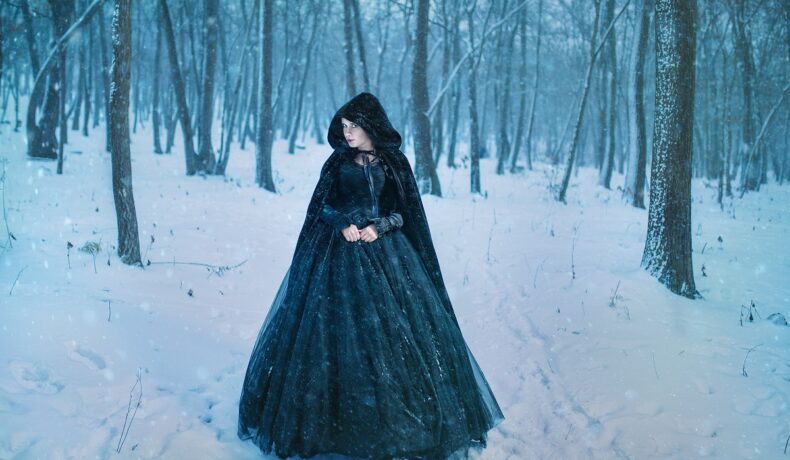 O femeie frumoasă într-o rochie neagră în timp ce se plimbă printr-o pădure cu zăpadă pentru a ilustra una dintre cele trei zodii răzbunătoare în ziua de 23 ianuarie 2023