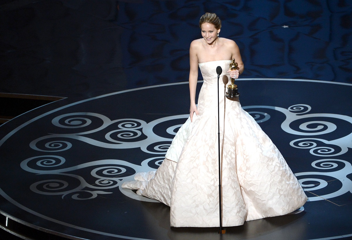 Jennifer Lawrence pe scena Premiilor Oscar 2013 poartă o rochie de culoare roz deschis