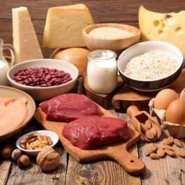 Mai multe alimente bogate în proteine sunt așezate pe o masșă de lemn precum ouăle, carnea și lactatele