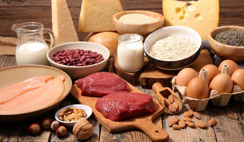 Mai multe alimente bogate în proteine sunt așezate pe o masșă de lemn precum ouăle, carnea și lactatele