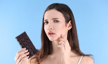O femei frumoasă care ține o tabletă de ciocolată și suferă de acnee