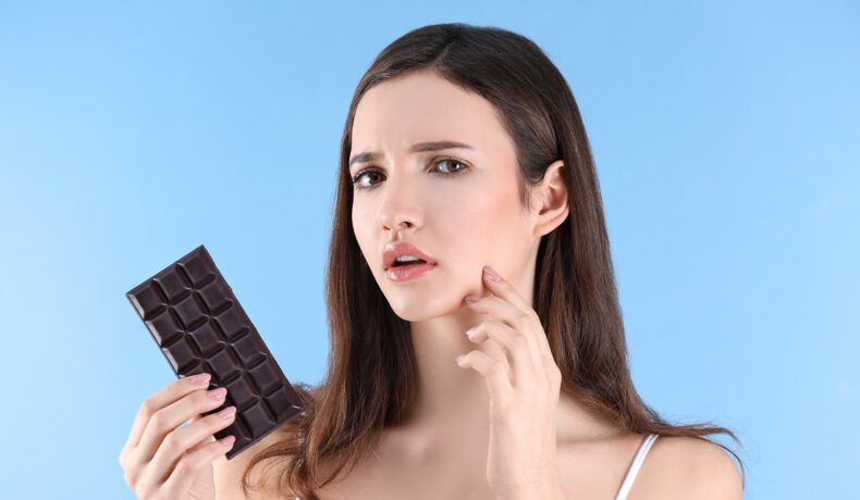 O femei frumoasă care ține o tabletă de ciocolată și suferă de acnee