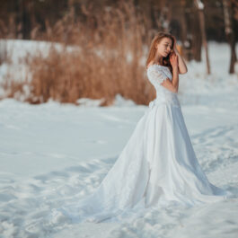 Fată frumoasă îmbrăcată într-o rochie albă stă în zăpadă