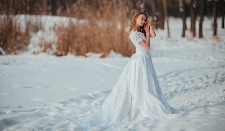 Fată frumoasă îmbrăcată într-o rochie albă stă în zăpadă