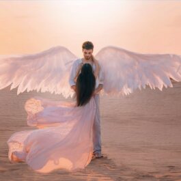 Un cuplu format dintr-o femeie și un bărbat poartă haine vaporoase de culoare albă, iar personajul masculin are aripi de înger