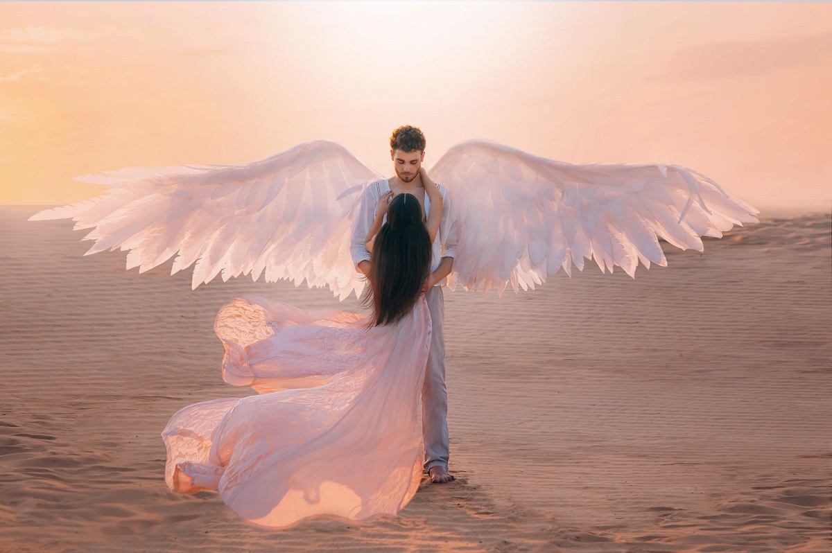 Un cuplu format dintr-o femeie și un bărbat poartă haine vaporoase de culoare albă, iar personajul masculin are aripi de înger