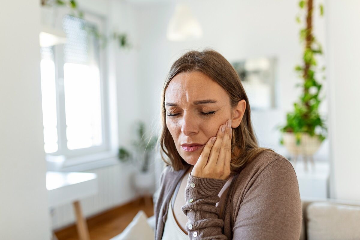 O femeie se plânge de o durere puternică de dinți și ține mâna stângă deasupra obrazului