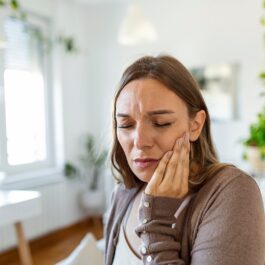 O femeie se plânge de o durere puternică de dinți și ține mâna stângă deasupra obrazului