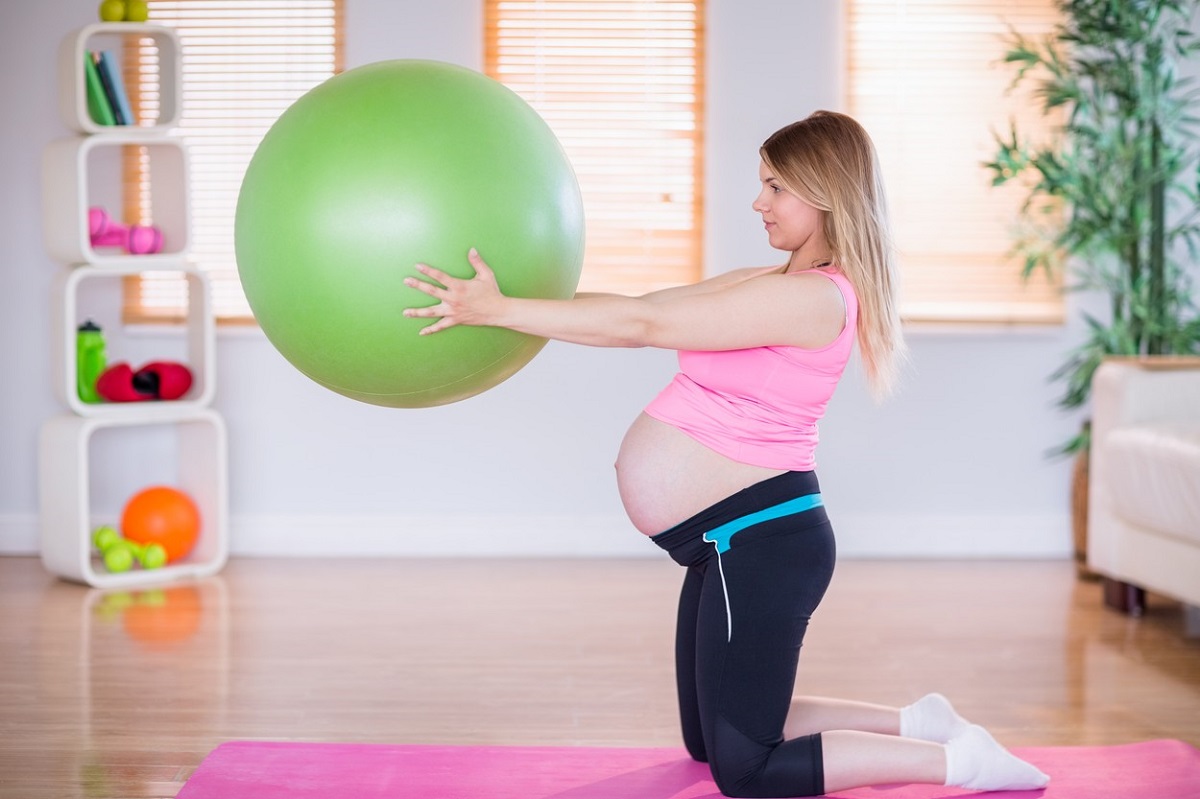 O femeie tânără, însărcinată folosește o minge pentru exerciții fizice