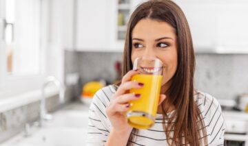 O femeie tânără care zâmbește consumă un pahar de suc de portocale natural