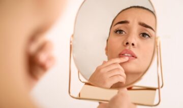 O femeie tânără și frumoasă stă mirată în fața unei oglinzi, îngrijorată de buzele sale crăpate